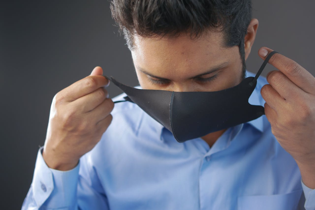 Man in blue shirt putting on a face mask for safety and health protection.