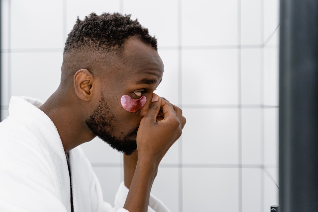 Side view of a man applying under eye mask, focusing on skincare routine.